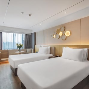Habitació d'hotel amb dos llits, zona de seients, llum penjada a la paret i finestra amb cortines.