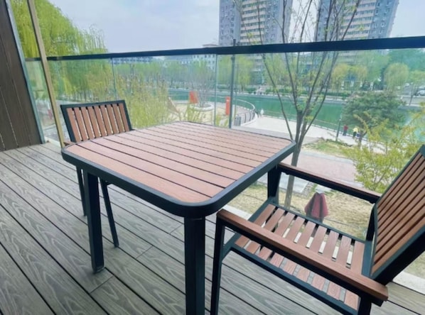 Un balcón con una mesa y dos sillas, con vistas a un parque y edificios.