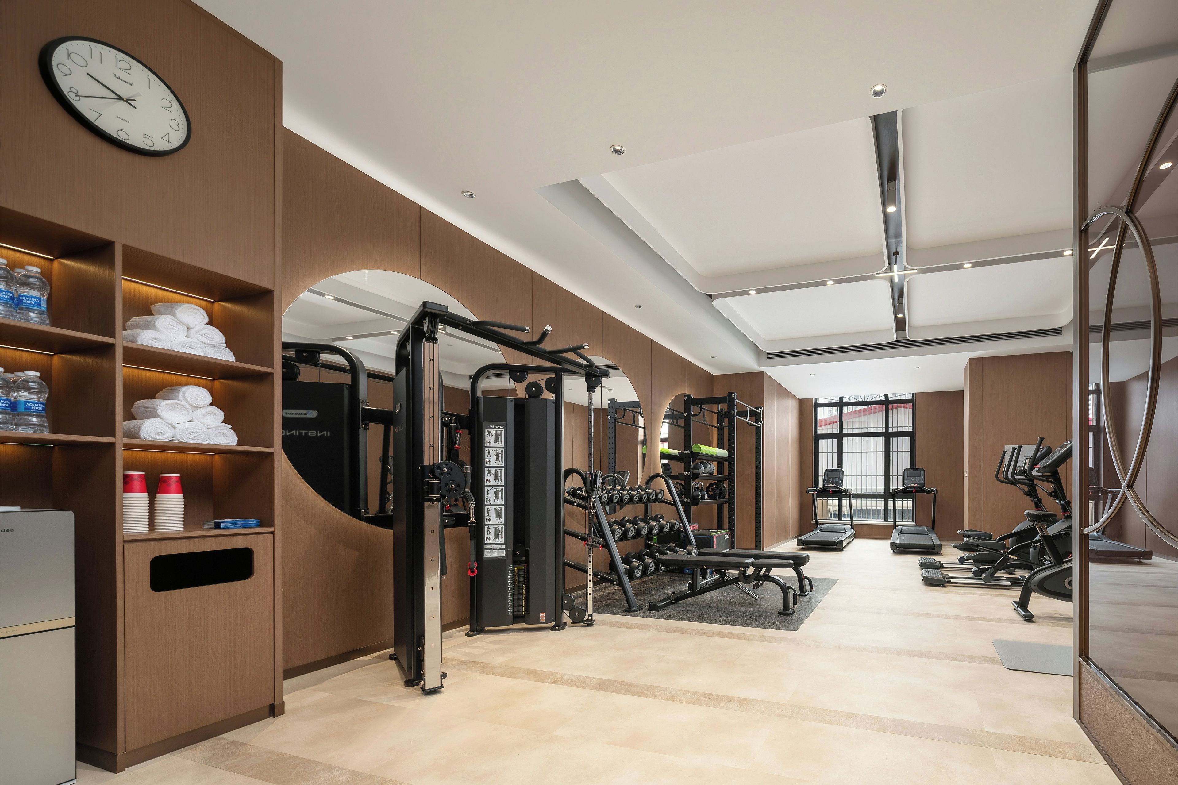 A modern gym with exercise equipment, a clock, and neatly arranged towels.