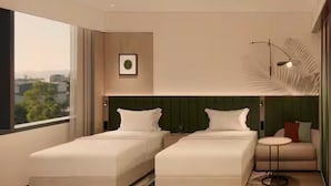 Ein modernes Hotelzimmer mit zwei Betten, einer kleinen Sitzecke, einem großen Fenster und einer Wanddekoration.