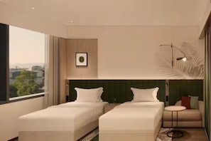 Et moderne hotelværelse med to senge, et lille siddeområde, et stort vindue og en dekorativ vægdekoration.