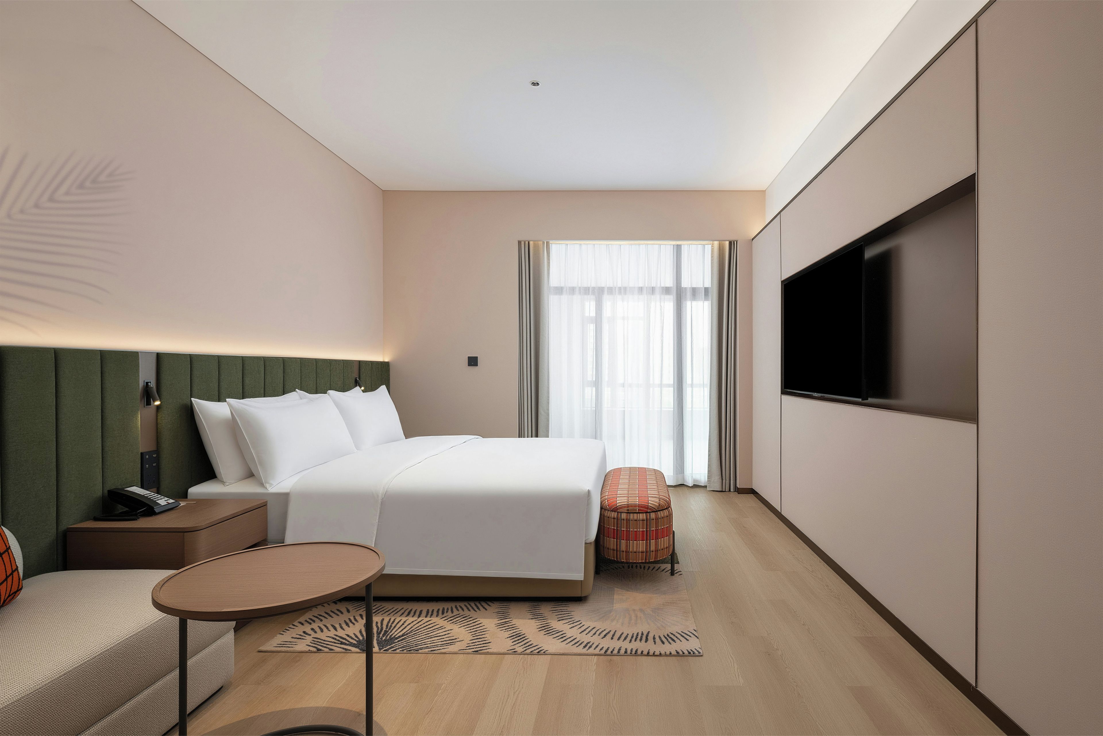 Quarto de hotel moderno com cama, mesa de cabeceira, abajur, televisão e uma pequena mesa redonda.