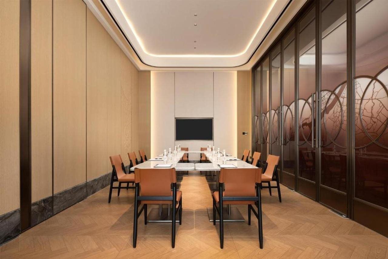 Une salle de conférence équipée d’une longue table, de chaises, d’un téléviseur à écran plat et d’une cloison en verre ornée d’un motif décoratif.