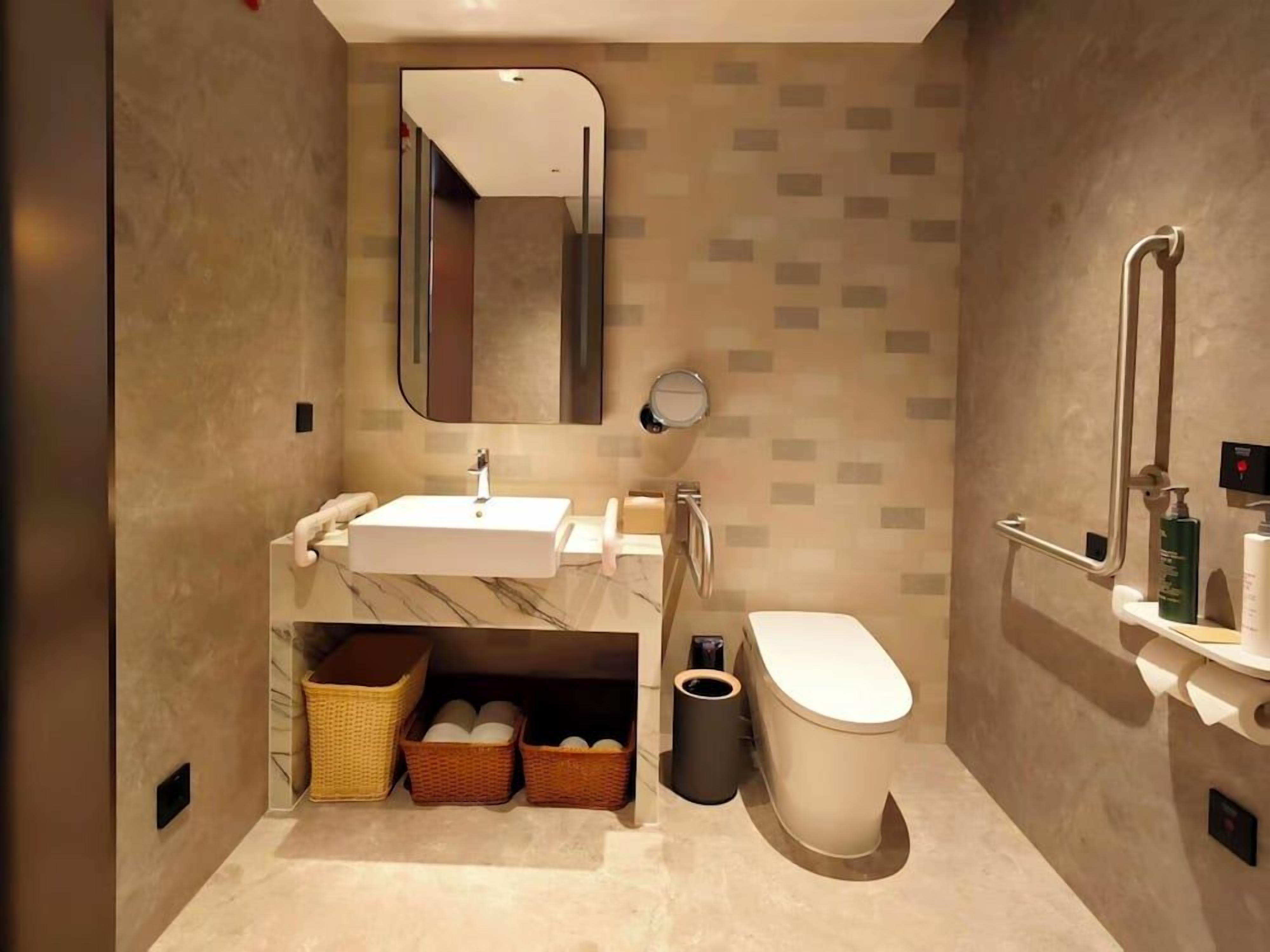 A modern bathroom with a sink, mirror, toilet, and storage baskets.