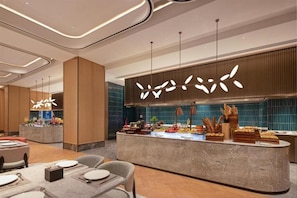 Una hall d'albergo moderna con un'area buffet centrale, diverse disposizioni di posti a sedere e lampade dal design contemporaneo.