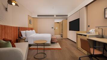 A modern hotel room with a bed, a desk, a chair, a small table, and a TV.