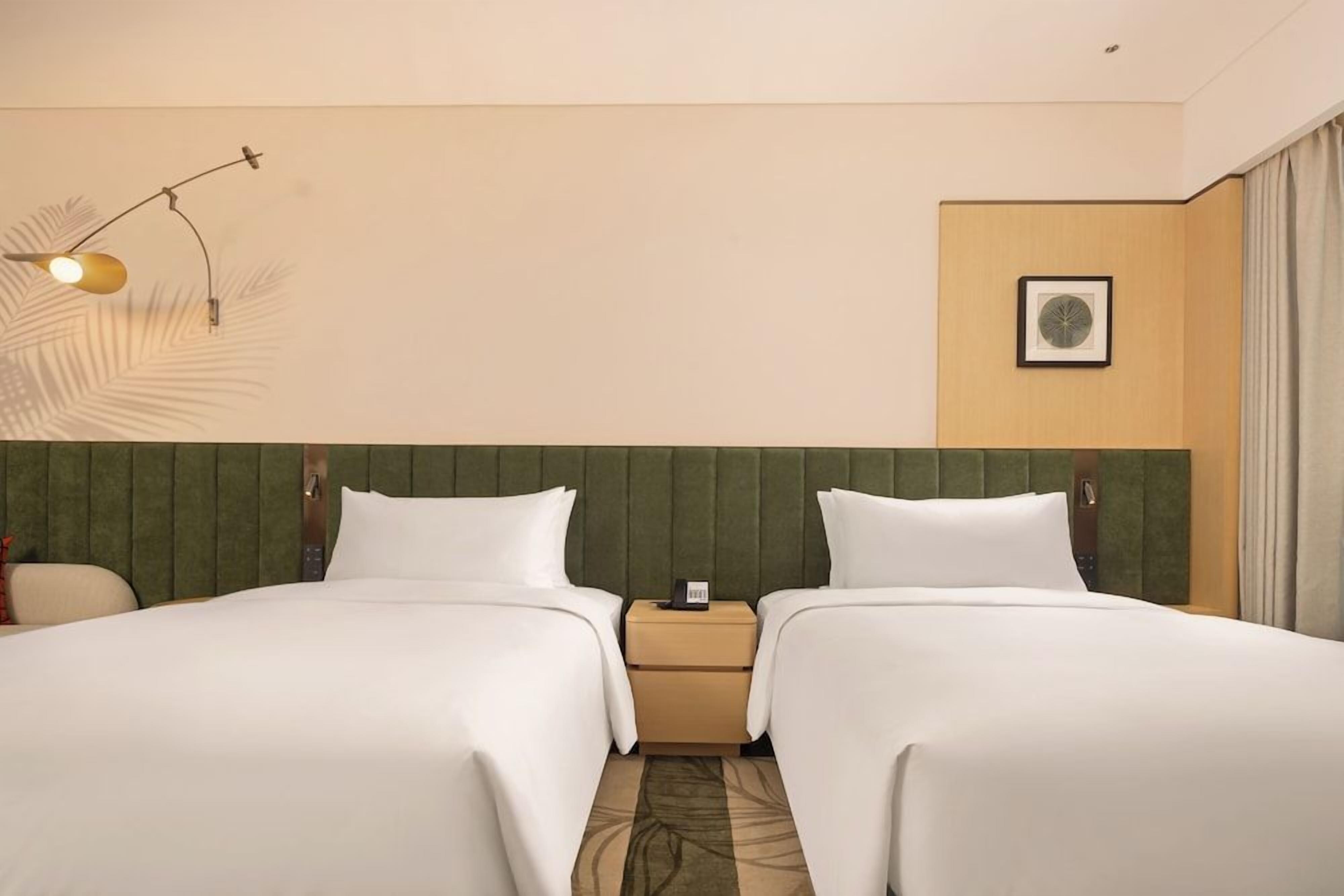 A hotel room with two beds, a nightstand, a lamp, and a framed picture on the wall.