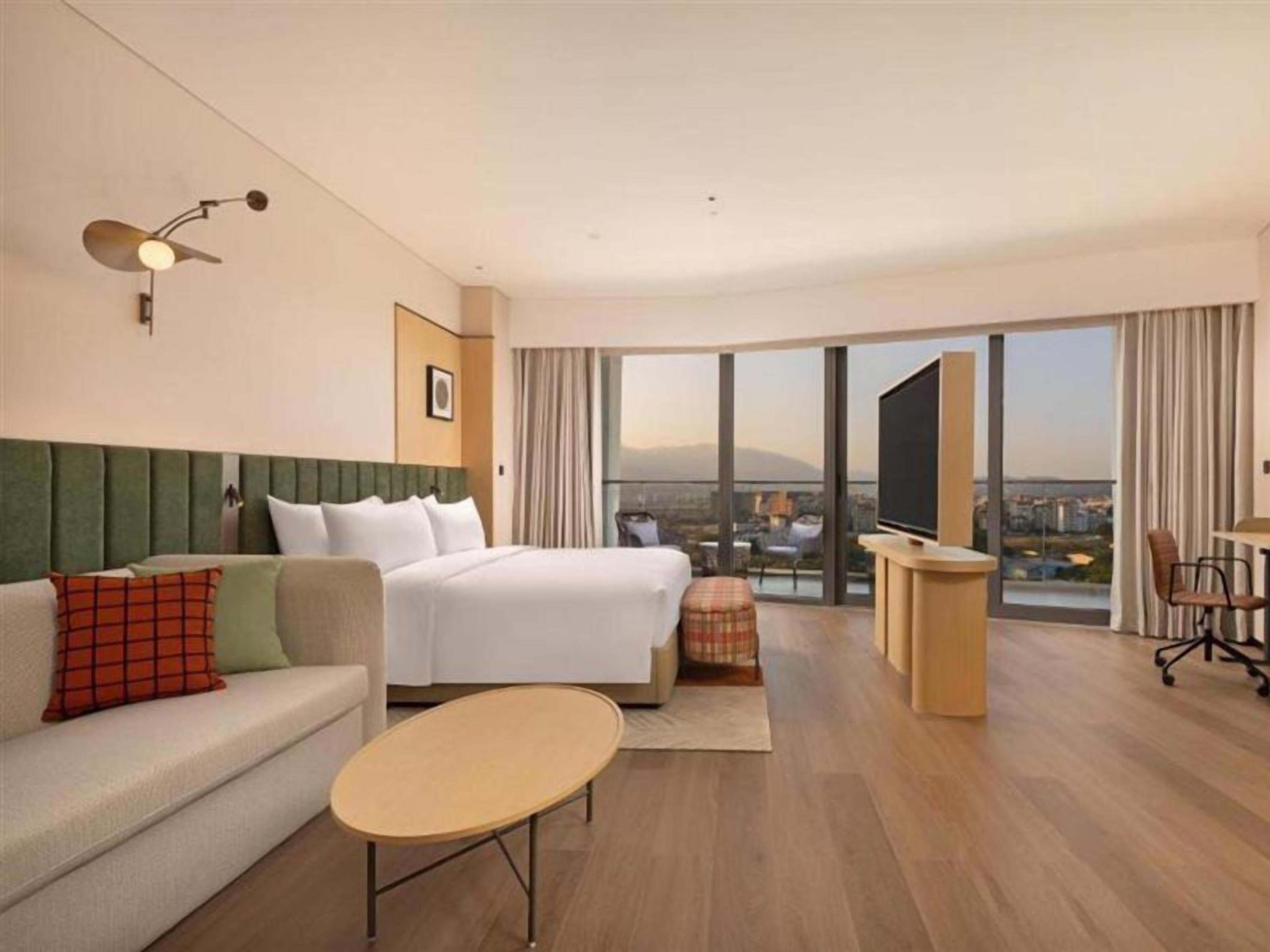 A hotel room with a bed, a sofa, a desk, and a view of the city.
