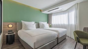 A hotel room with two beds, a round wall clock, a small table, and a chair.