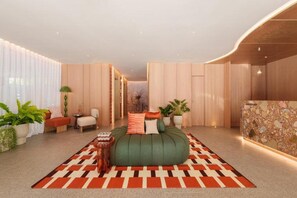 A modern hotel room with a green sofa bed, a patterned rug, and a stone accent wall. - The Akyra Bangkok 11 (Bangkok)