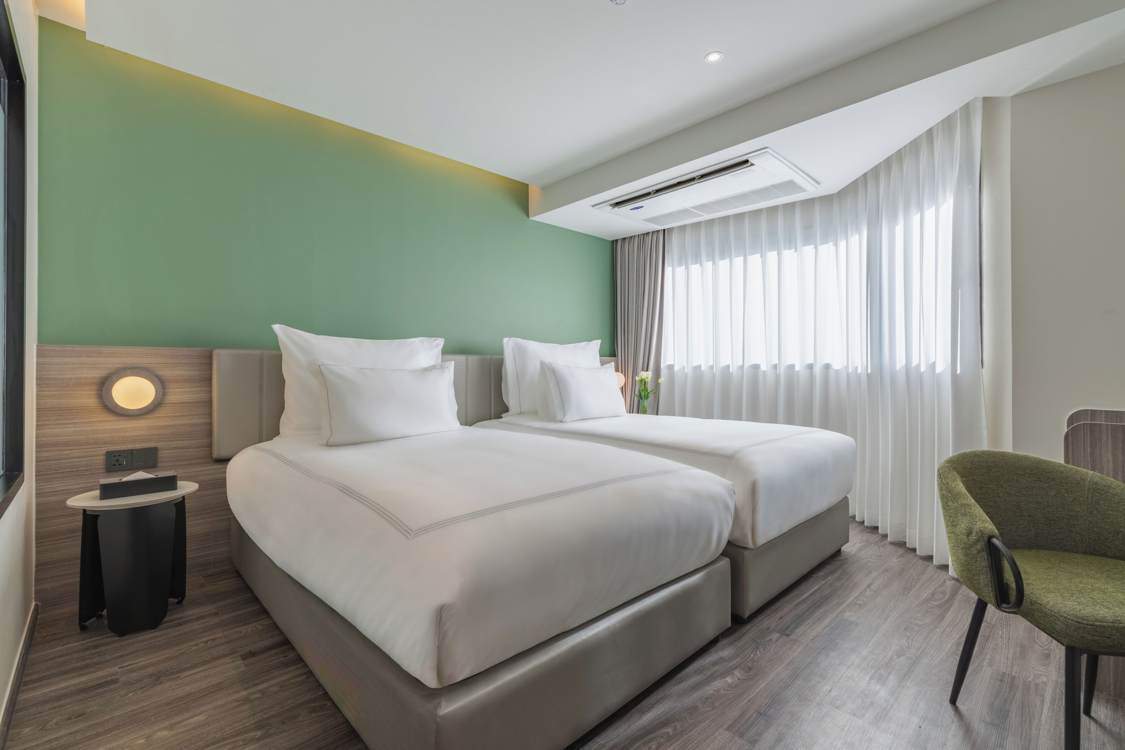A hotel room with two beds, a small table, a chair, and a large window with curtains.