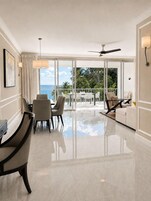 Una habitación de hotel moderna con zona de comedor, sofá y balcón con vista al océano.