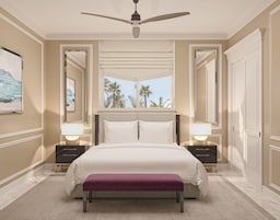 Un dormitorio de hotel con una cama grande, lámparas de noche, ventilador de techo y vistas a palmeras.