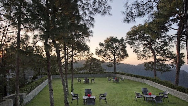 An outdoor seating area with tables and chairs, surrounded by trees and a stone wall. - Fortune Select Forest Hill Kasauli (Solan)