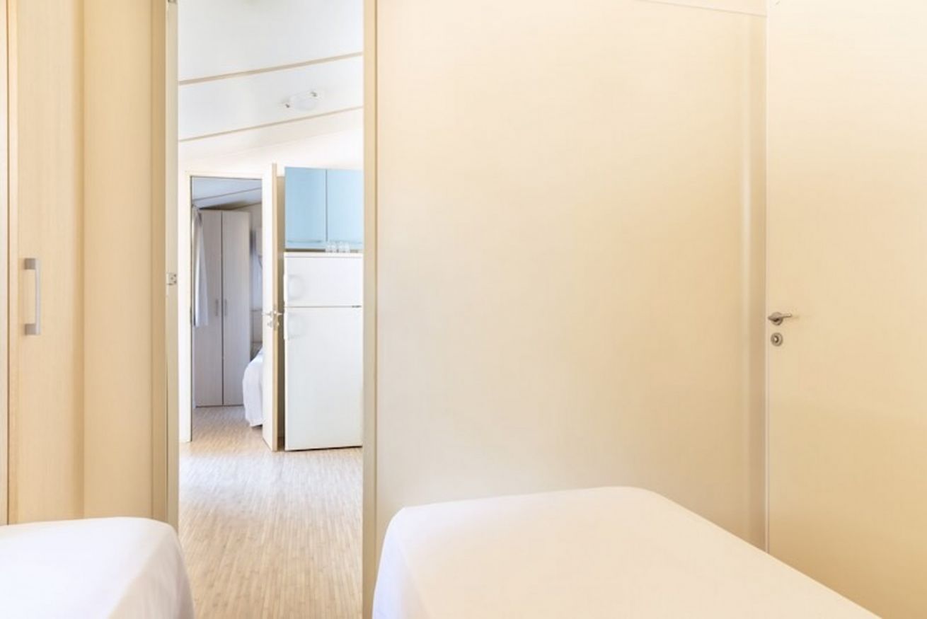 Una camera d'albergo con due letti, un ingresso per il bagno e vista su un'area cucina.