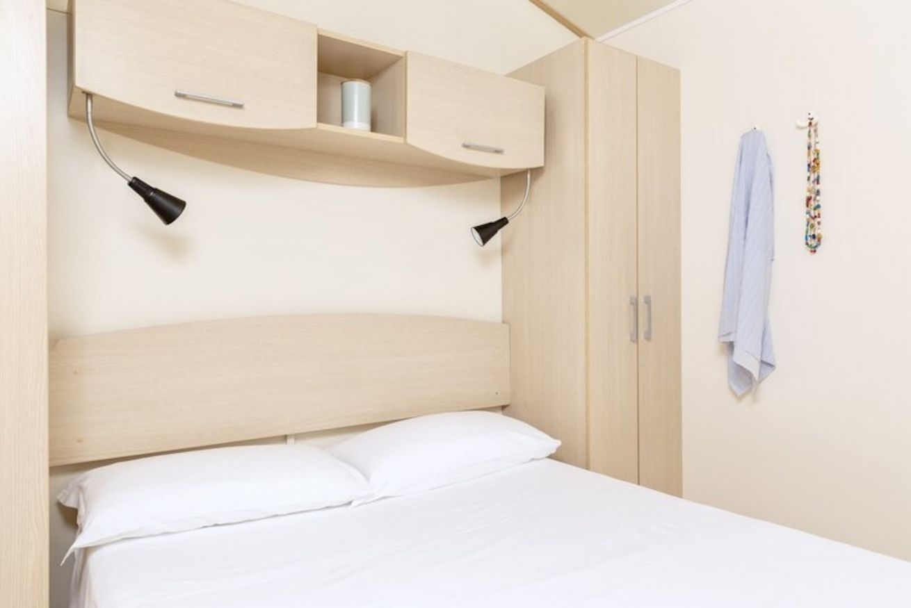 A bedroom with a bed, a headboard, a wardrobe, and two wall-mounted lamps.