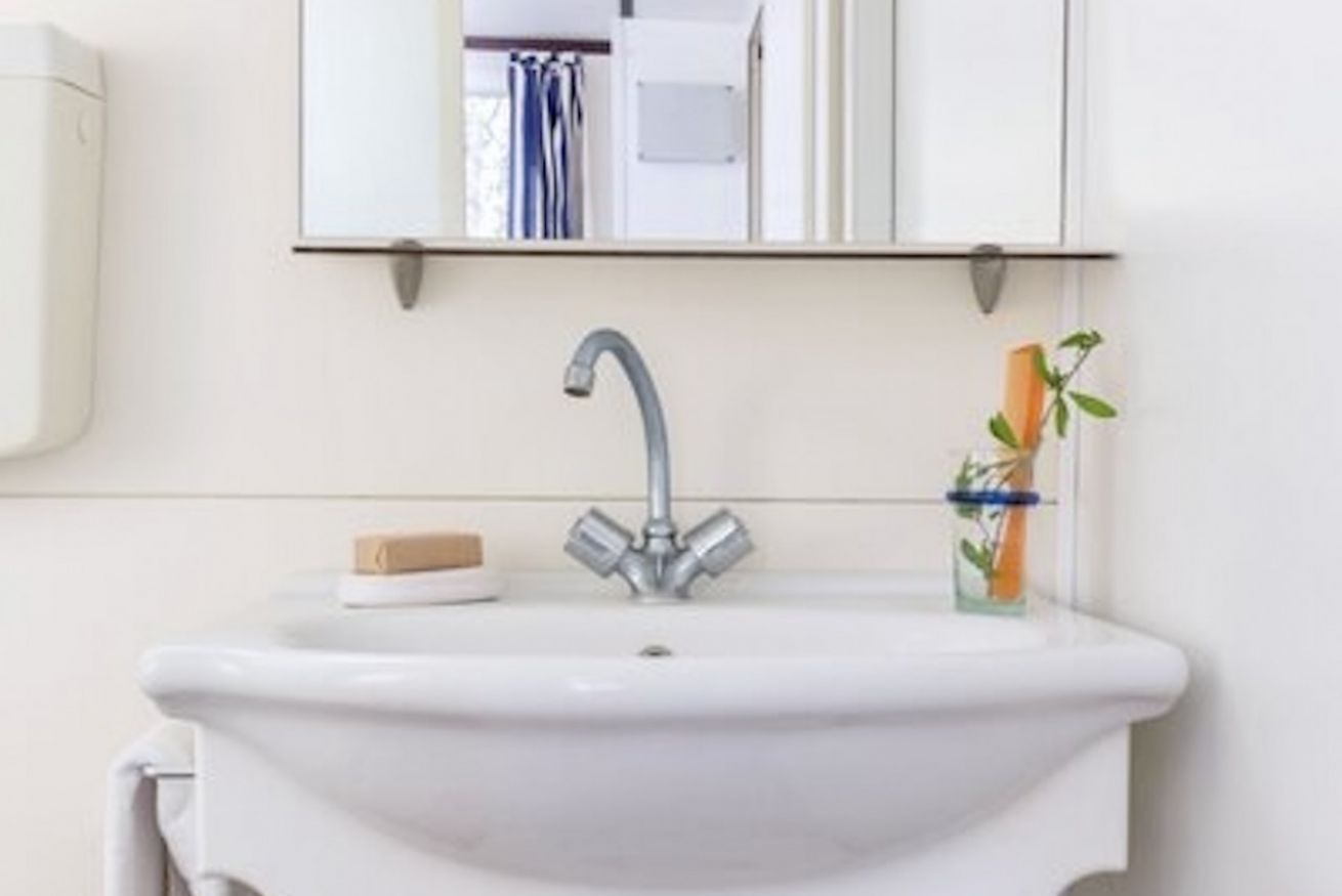 Une salle de bain avec un lavabo blanc, un miroir au-dessus et un porte-serviettes à gauche.