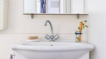 Une salle de bain avec un lavabo blanc, un miroir au-dessus et un porte-serviettes à gauche.