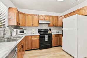 A kitchen with wooden cabinets, a stainless steel sink, a white refrigerator, a black stove, and a microwave. - Island Cottage, Fenced Yard, Huge Porch, Game Room, Fire Pit, Walk/Bike Downtown, $300 Free Tickets! (St. Augustine)