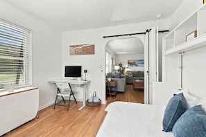A modern bedroom with a bed, a desk with a computer, and a view of another room. - Island Cottage, Fenced Yard, Huge Porch, Game Room, Fire Pit, Walk/Bike Downtown, $300 Free Tickets! (St. Augustine)