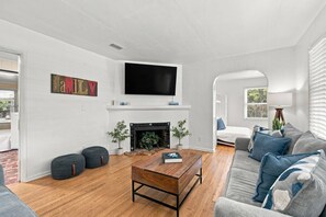 A living room with a fireplace, a flat-screen TV, a sofa, and a coffee table. - Island Cottage, Fenced Yard, Huge Porch, Game Room, Fire Pit, Walk/Bike Downtown, $300 Free Tickets! (St. Augustine)