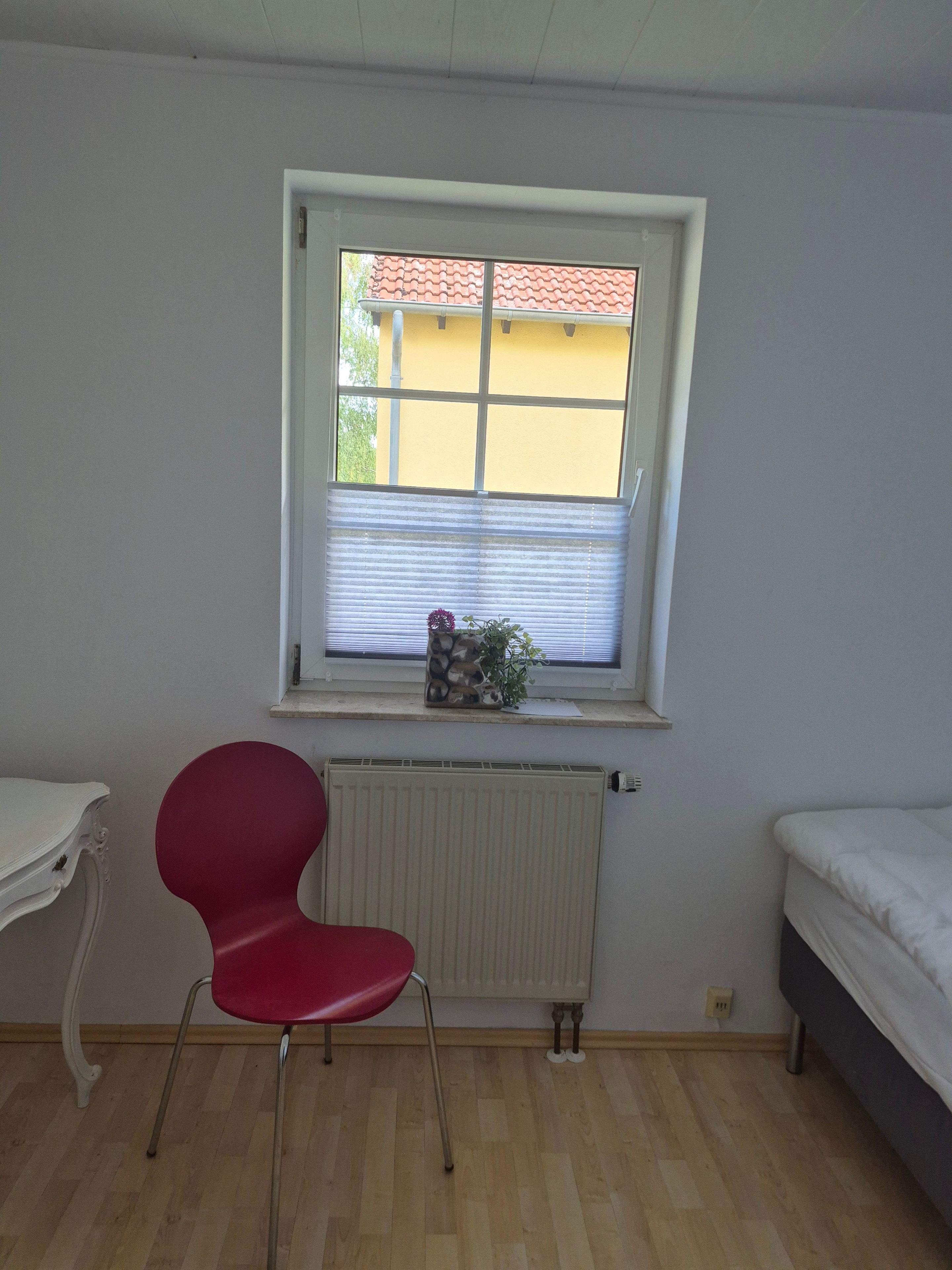 A room with a window, a radiator, a red chair, and a bed.