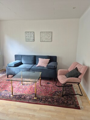A living room with a blue sofa, a glass coffee table, a pink armchair, and a patterned rug. - Apartment 'Am Golfplatz' with Wi-Fi (Baustert)