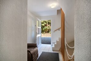 A hallway with a brown sofa, a staircase with a wooden handrail, and a door leading outside. - Apartment 'Am Golfplatz' with Wi-Fi (Baustert)
