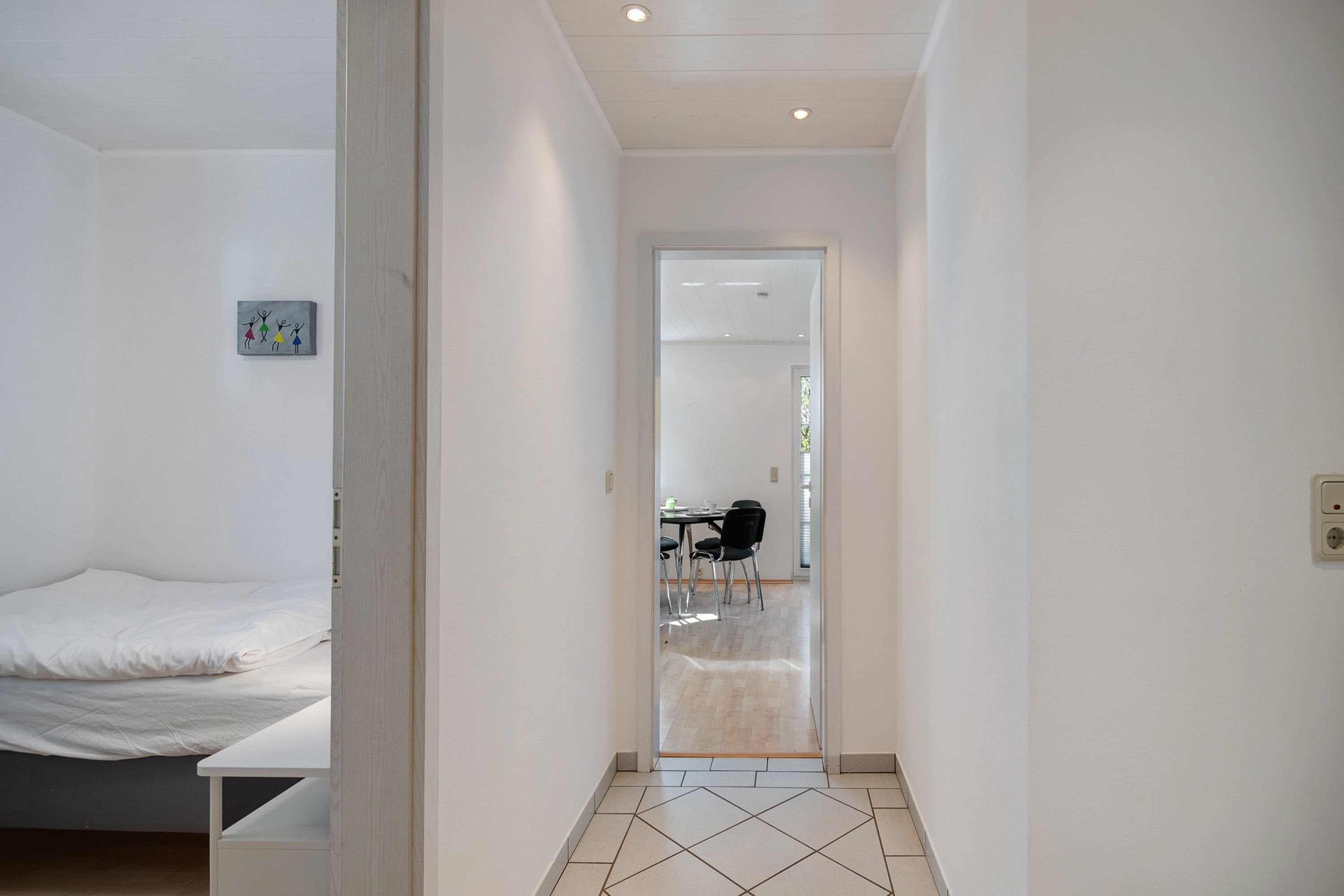 A bedroom with a bed, a small artwork, and a hallway leading to a dining area.