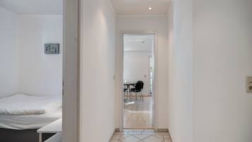 A bedroom with a bed, a small artwork, and a hallway leading to a dining area.