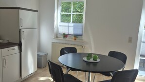 Een moderne keuken met witte kasten, een inbouwkoelkast en een raam met zonwering.