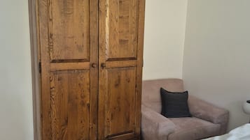 Ein Zimmer mit einem Holzschrank, einem Bett mit weißer Bettwäsche und einem rosafarbenen Sofa mit einem dunkelgrauen Kissen.