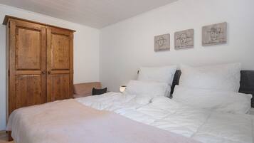 Une chambre avec une grande armoire en bois, un lit avec une literie blanche et trois œuvres d’art accrochées au mur.