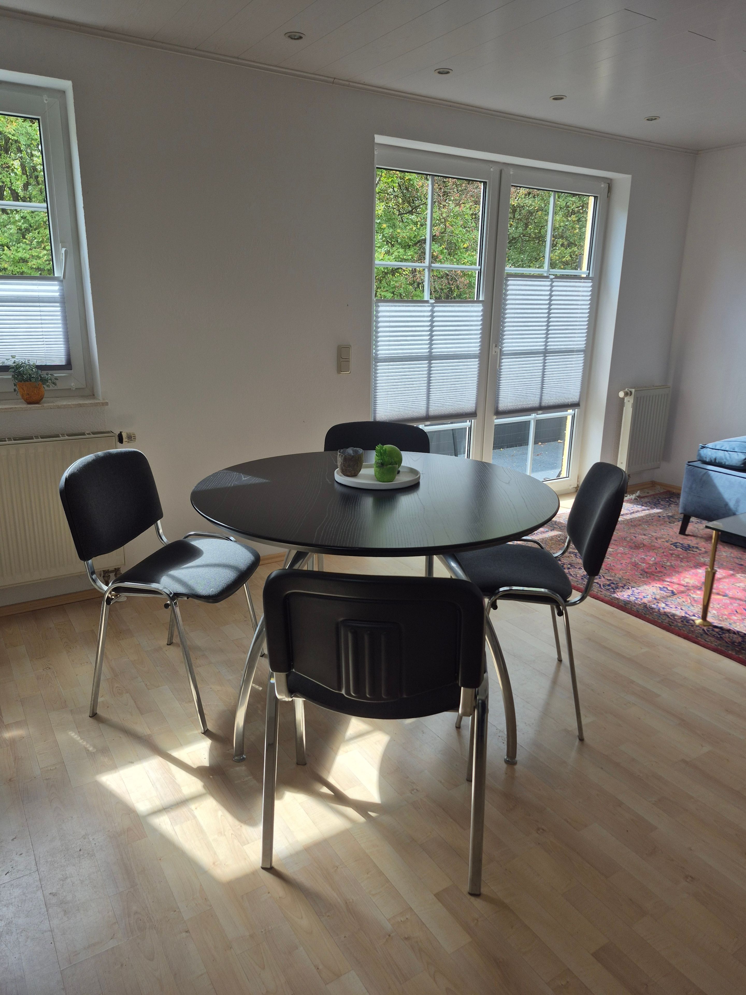 Ein Essbereich mit einem runden Tisch, vier Stühlen und einem Fenster mit Jalousien.