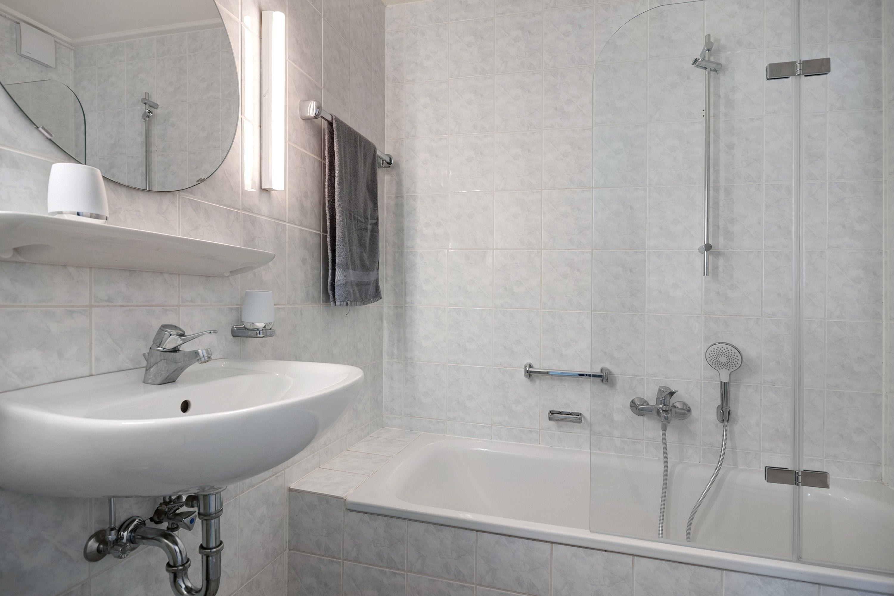 Ein modernes Badezimmer mit einem weißen Waschbecken, einer Duschkabine aus Glas und einem Spiegel über dem Waschbecken.