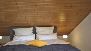 Une chambre à coucher avec un plafond en pente, un lit avec une literie grise et un oreiller jaune, ainsi que des lampes de chevet.