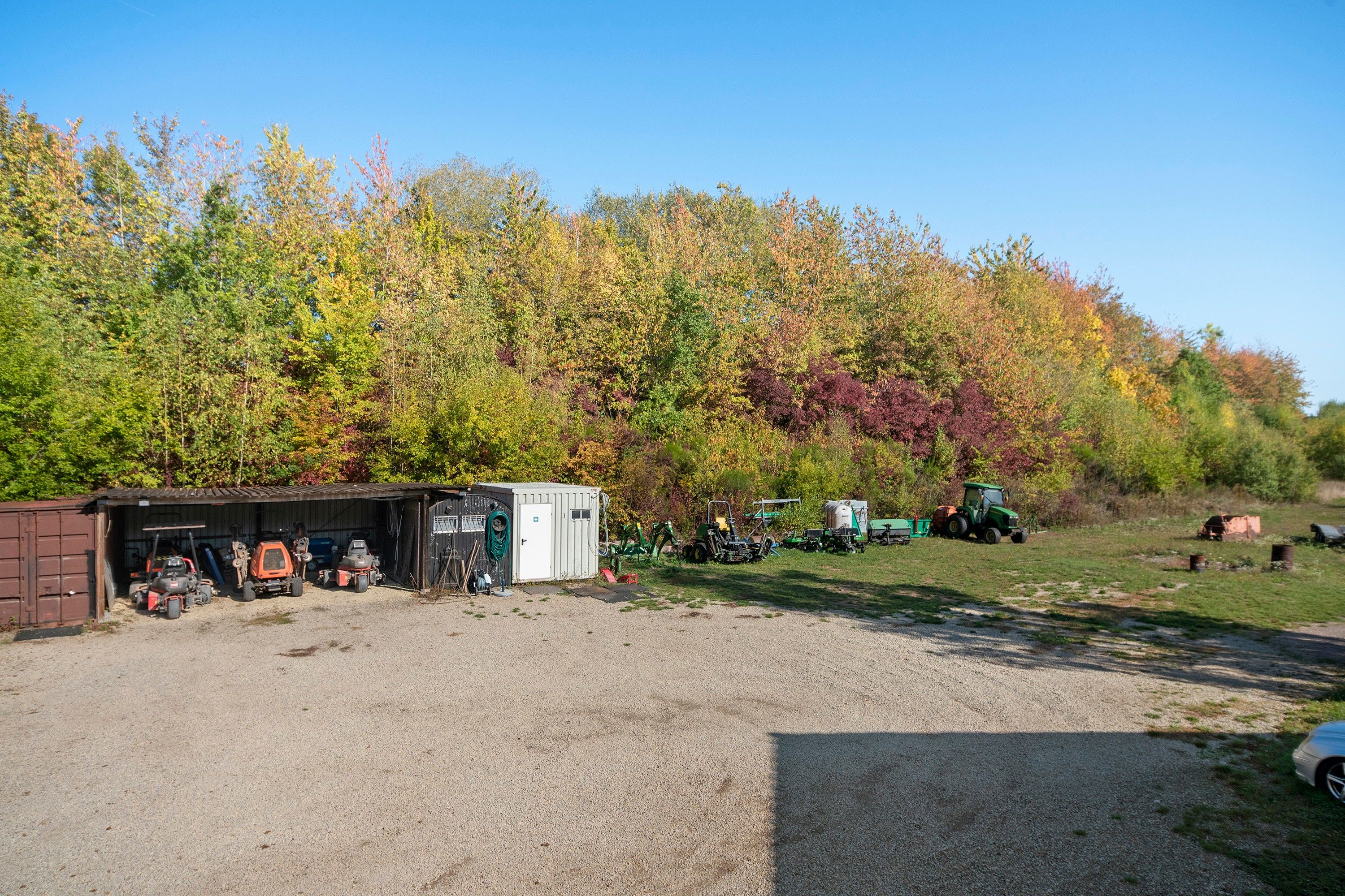 Un espace de stationnement recouvert de gravier, avec un petit abri et un tracteur.