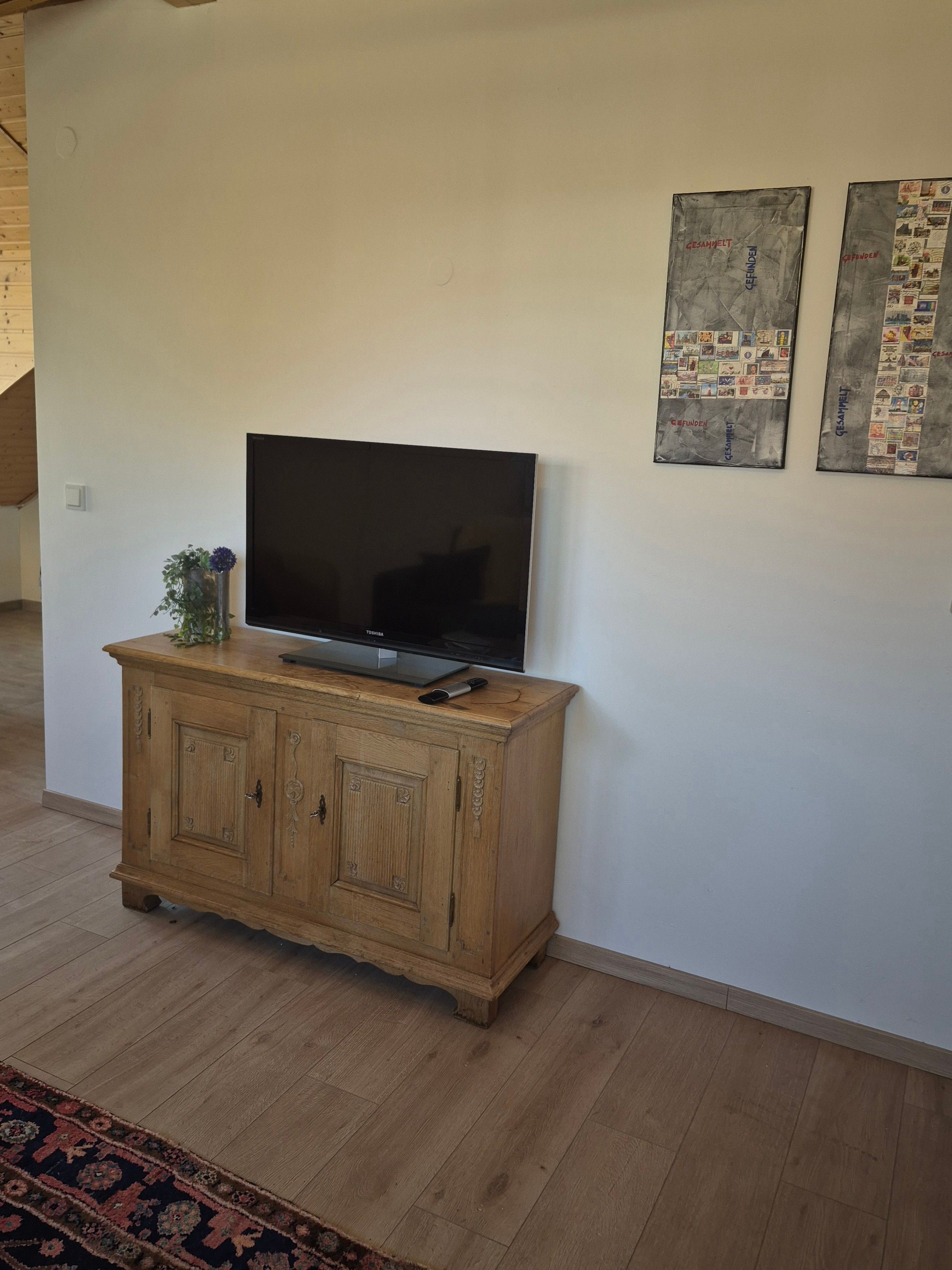 Ein Flachbildfernseher auf einer Holzkommode, eine kleine Pflanze und zwei gerahmte Bilder an der Wand.