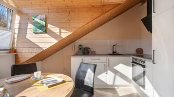 Une cuisine moderne avec un plafond en pente, un coin repas avec une table et des chaises, et une fenêtre avec des stores.