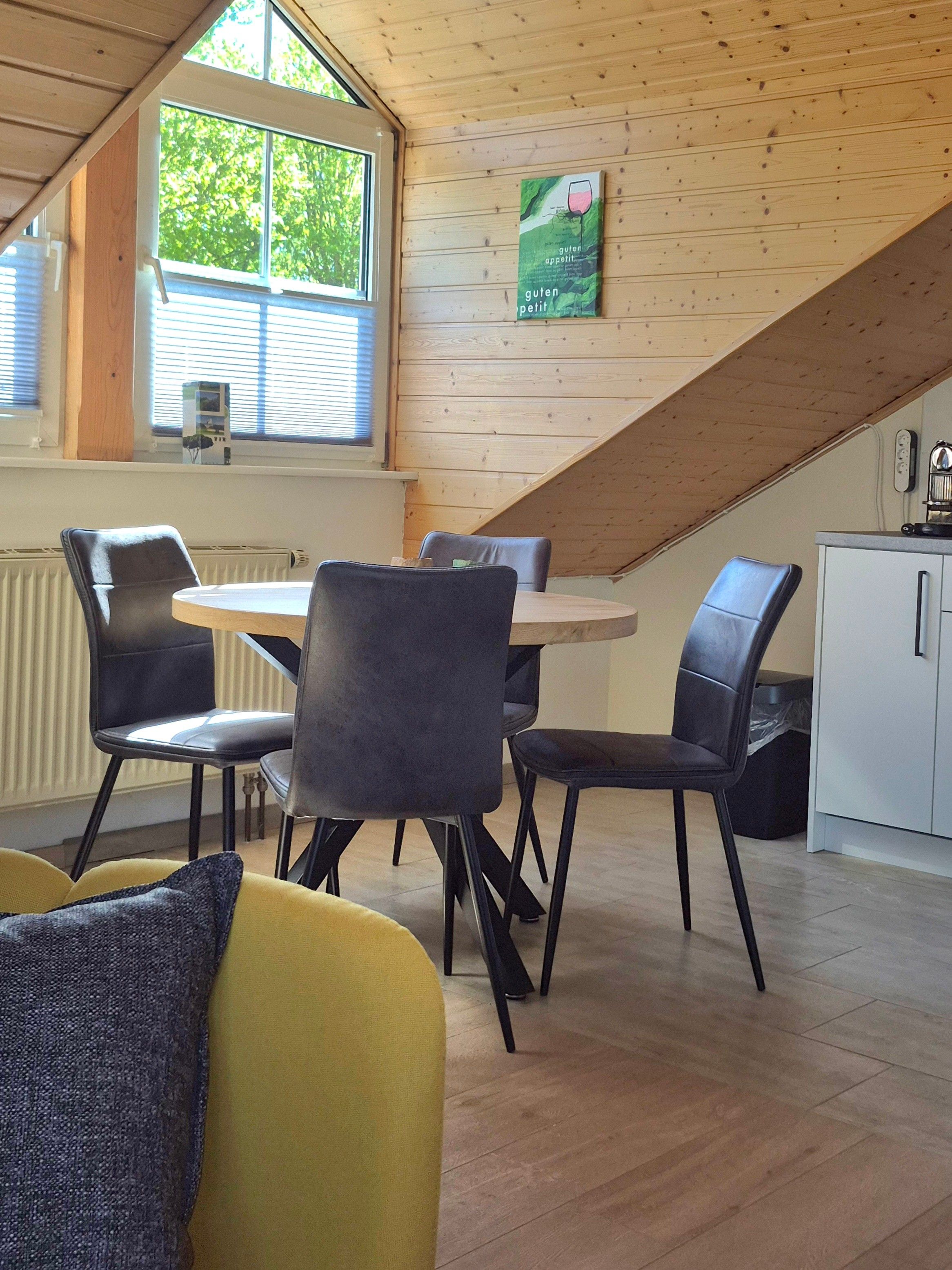 A dining area with a round table and four chairs, a kitchen area with a white cabinet, and a window with blinds.