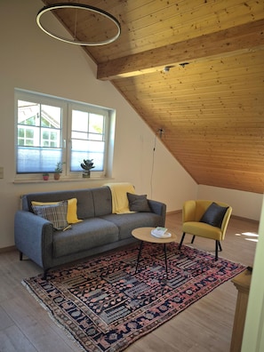 A room with a sloped ceiling, a sofa, a chair, a small table, and a patterned rug.