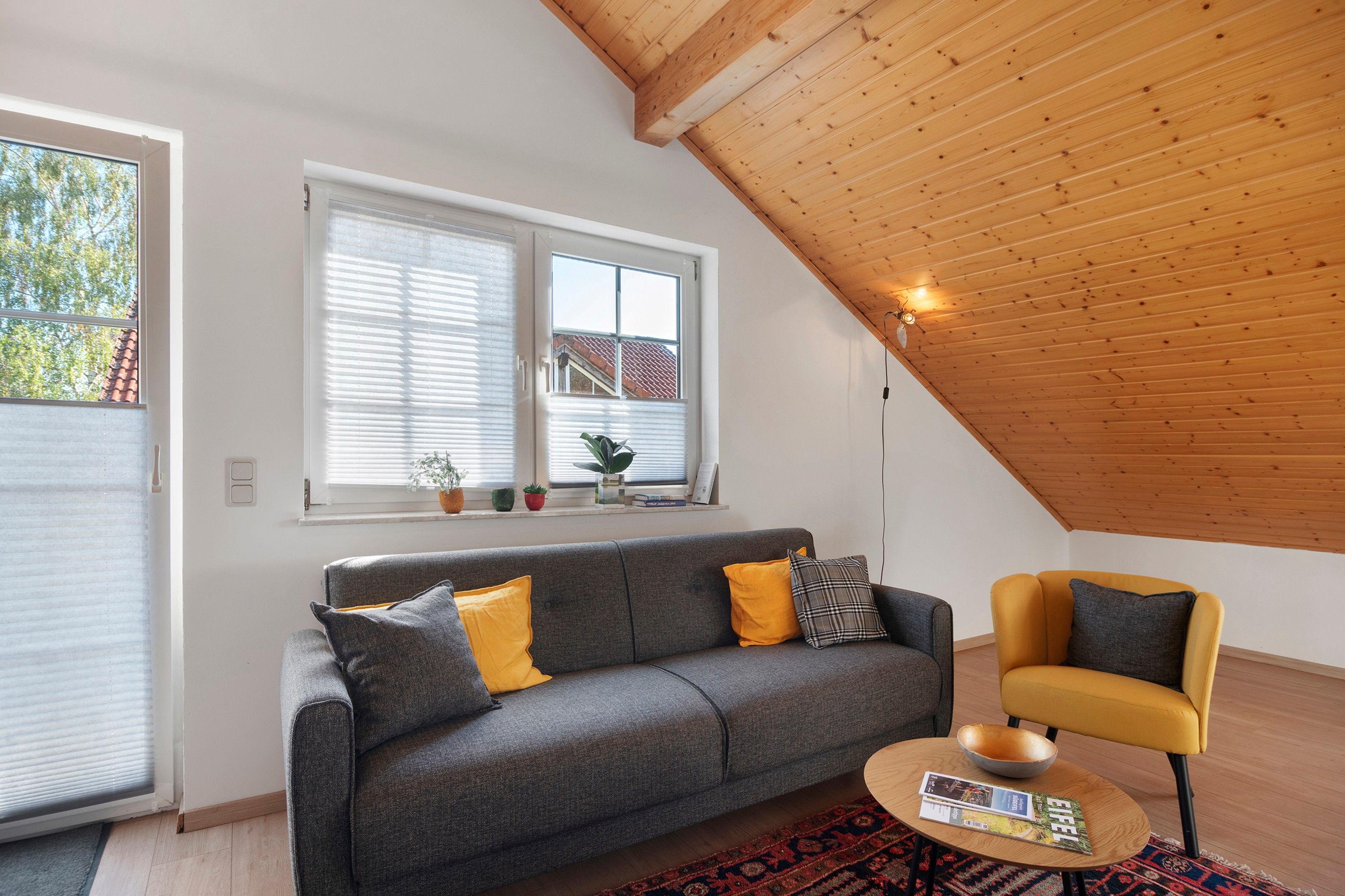 A modern living room with a grey sofa, a yellow armchair, and a wooden ceiling.