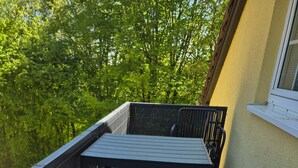 Un balcon avec une table et deux chaises, une vue sur la verdure et la façade d’un immeuble.