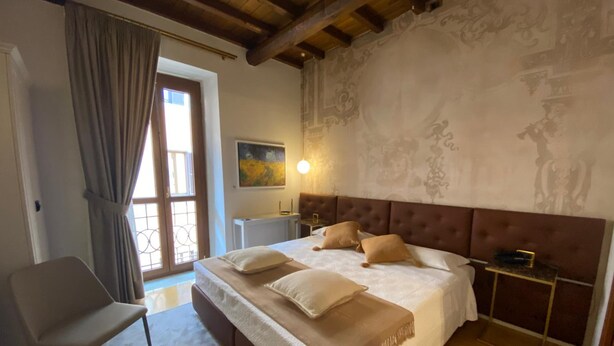 A bedroom with a large bed, a chair, a nightstand, and a window with curtains. - Rhona's Rooms B&B (Rome)