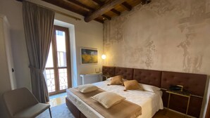 A bedroom with a large bed, a chair, a nightstand, and a window with curtains.