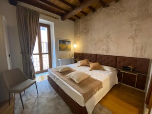A bedroom with a large bed, a chair, a nightstand, and a window with curtains. - Rhona's Rooms B&B (Rome)
