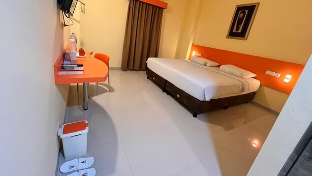 A hotel room with a bed, a desk, a chair, a trash bin, and a shower area. - New Waigo Hotel (Sorong)