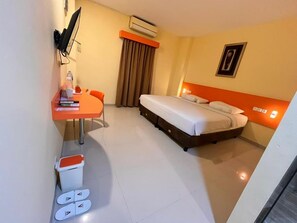 Habitación de hotel con cama, escritorio, silla, cesto de basura y zona de ducha.