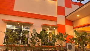 A building with a red and white facade, large windows, and a small garden area with plants. - New Waigo Hotel (Sorong)