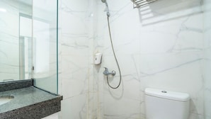 A bathroom with a glass shower enclosure, a marble wall, and a white toilet. - Life Hotel Sidoarjo (Sidoarjo)